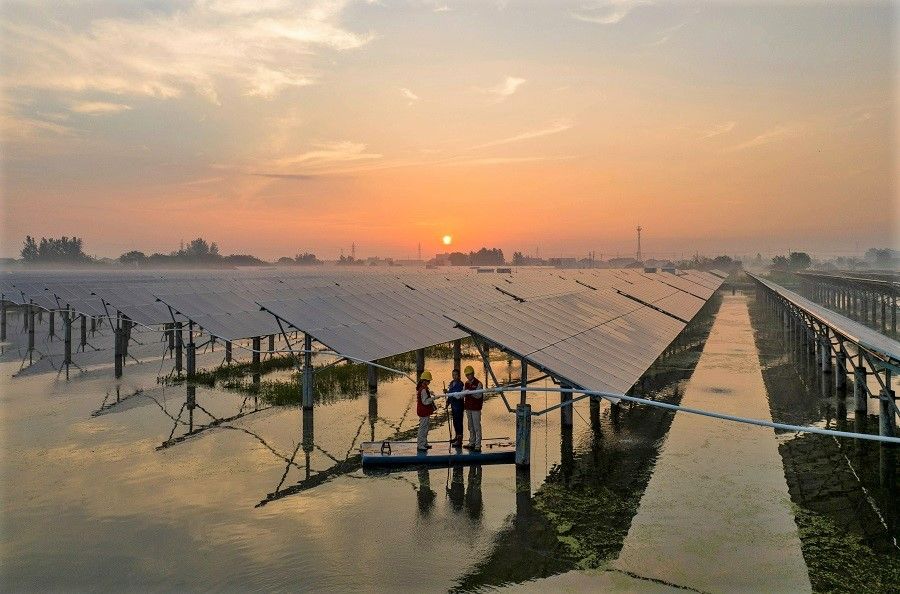 Workers inspect solar panels in the early morning at the fishing-solar complementary photovoltaic power generation base in Taizhou, Jiangsu province, China, on 12 July 2023. (Stringer/AFP)