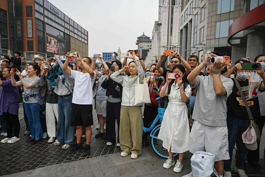 People take photos as US President Donald Trump’s motorcade passes the Wangfujing shopping street on the way to the airport after Trump met with Chinas President Xi Jinping in Beijing on 15 May 2026.
