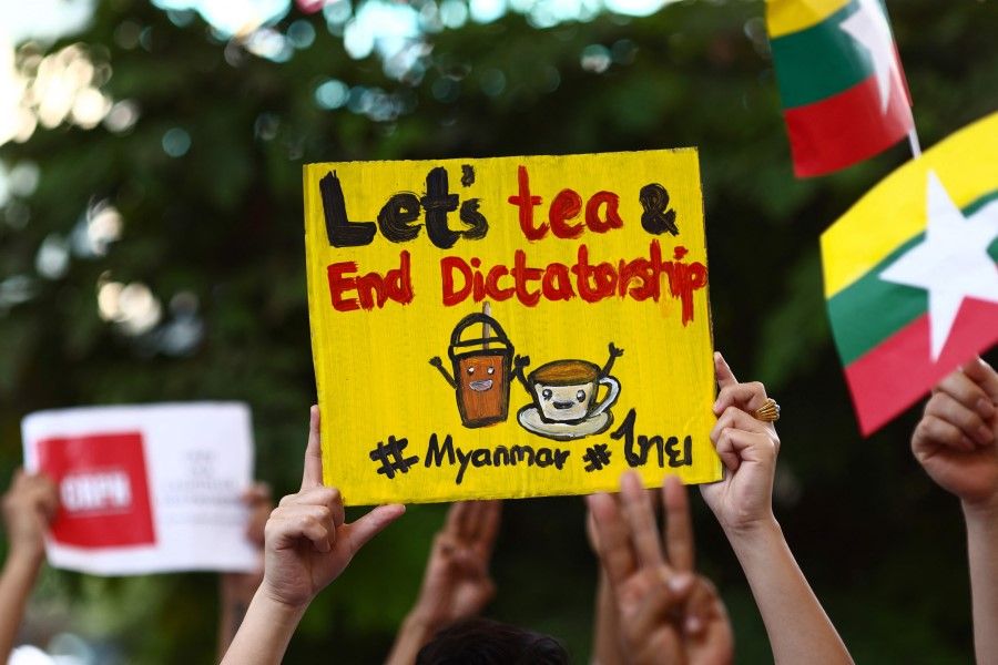Myanmar migrants in Thailand holds signs relating to the "Milk Tea Alliance" as they take part in a protest in Bangkok on 28 February 2021, against the military coup in their home country. (Jack Taylor/AFP)