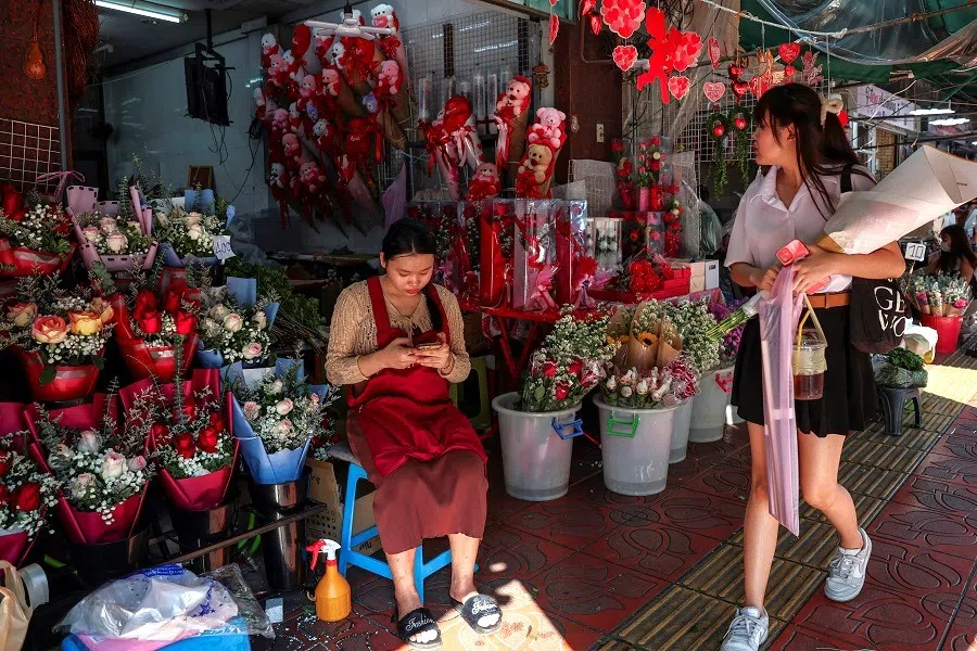 A woman carrying a bouquet walks past a flower shop at a market in Bangkok, Thailand, on 13 February 2025. (Chalinee Thirasupa/Reuters)