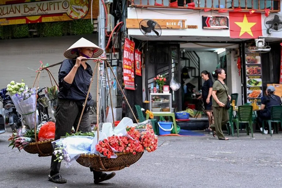 A street vendor carries bouquets of flowers for sale in Hanoi on 22 October 2025.