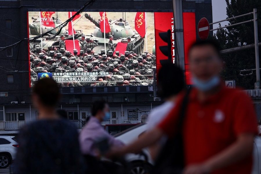 Pedestrians walk past a screen showing footage of Chinese People's Liberation Army (PLA) soldiers during an evening news programme, in Beijing, China, 2 August 2022. (Tingshu Wang/Reuters)