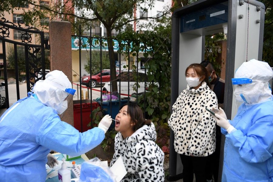 A medical worker in protective suit collects a swab from a resident at a free nucleic acid testing site following new cases of the coronavirus disease (COVID-19), in Lanzhou's Chengguan district, Gansu province, China, 20 October 2021. (cnsphoto via Reuters)