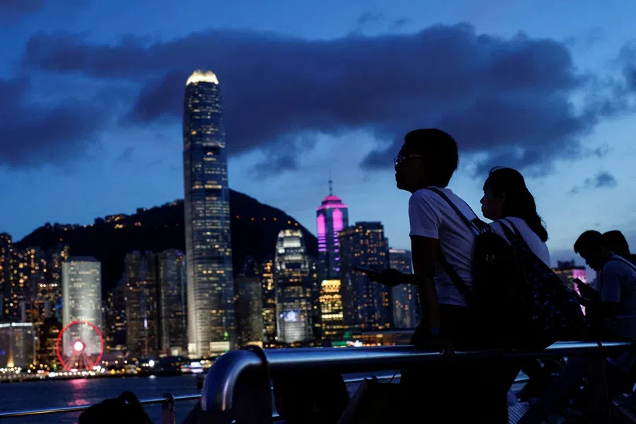 Tourists relax on the waterfront in front of Victoria Harbour, with the iconic skyline buildings as a backdrop, in Hong Kong, China on 28 June 2023. (Tyrone Siu/Reuters)