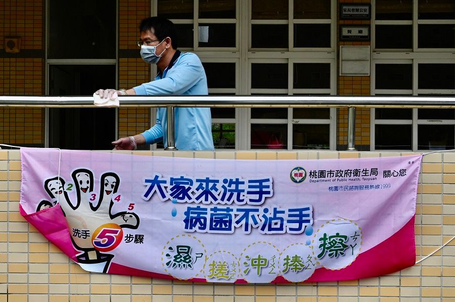 A man wearing a face mask cleans a handrail behind a sign telling students how to wash their hands amid the Covid-19 pandemic at a middle school in Taoyuan, Taiwan, on 29 February 2020. (Sam Yeh/AFP)