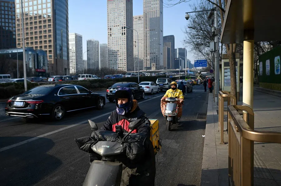 Food delivery men ride electric scooters along a street in the central business district in Beijing on 16 January 2024. (Wang Zhao/AFP)