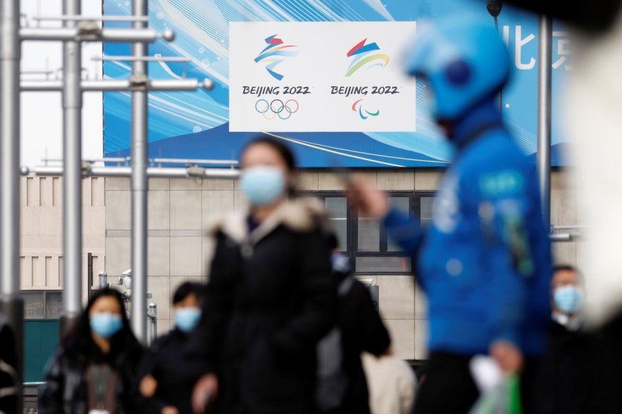 Pedestrians walk past the emblems of Beijing 2022 Winter Olympic and Paralympic Games near a flagship merchandise store for the Beijing 2022 Winter Olympics in Beijing, China, 8 December 2021. (Carlos Garcia Rawlins/Reuters)