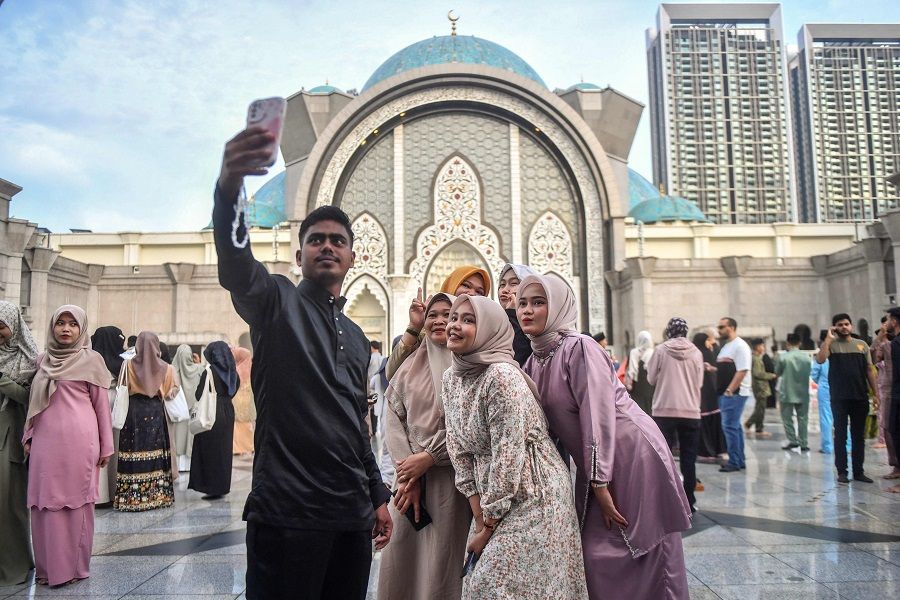 People take a selfie with the backdrop of the Federal Territory mosque in Kuala Lumpur on 10 April 2024, as they gather to perform Eid al-Fitre prayers marking the end of the holy month of Ramadan. (Arif Kartono/AFP)