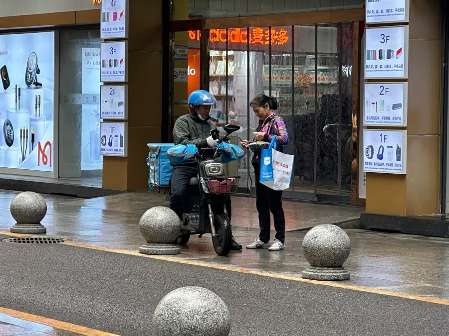A substitute delivery auntie helps a delivery rider deliver takeouts to a customer.