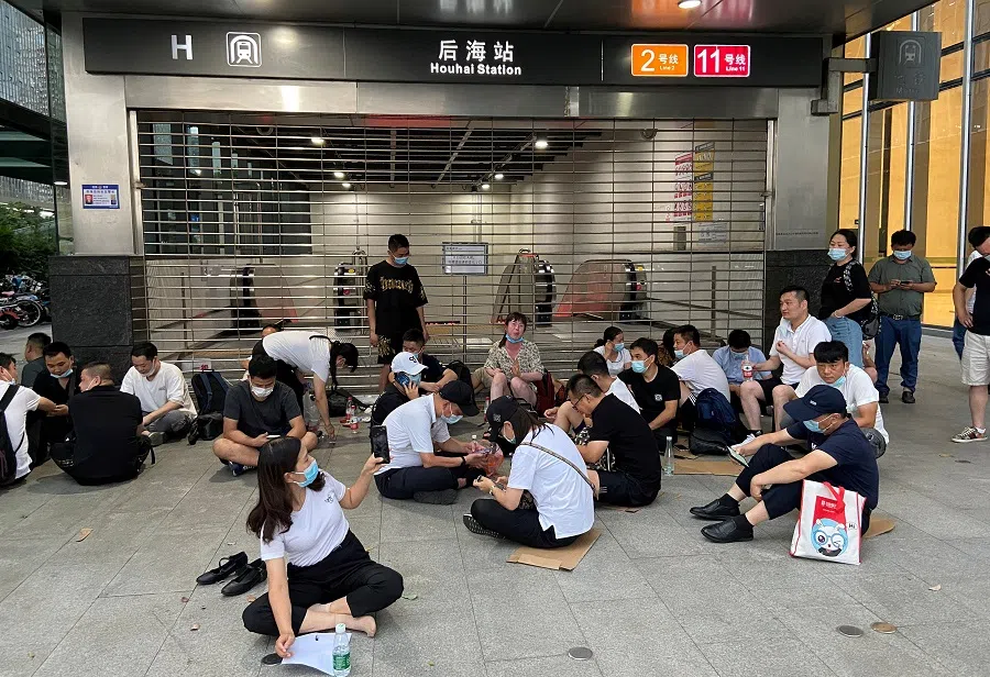 People sit under the shelter of a subway entrance next to Evergrande's headquarters, where they are demanding repayment of loans and financial products, in Shenzhen, Guangdong province, China, 16 September 2021. (David Kirton/Reuters)