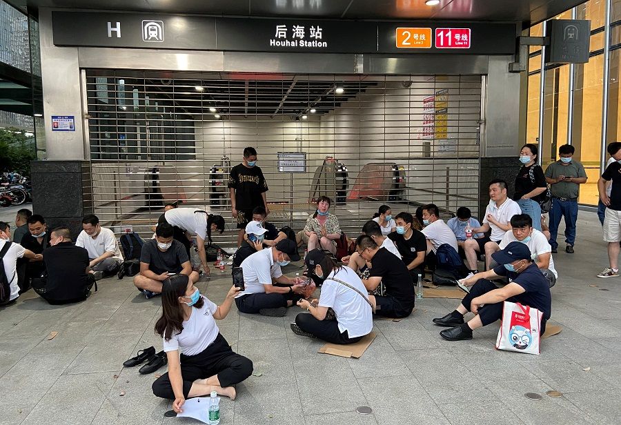 People sit under the shelter of a subway entrance next to Evergrande's headquarters, where they are demanding repayment of loans and financial products, in Shenzhen, Guangdong province, China, 16 September 2021. (David Kirton/Reuters)