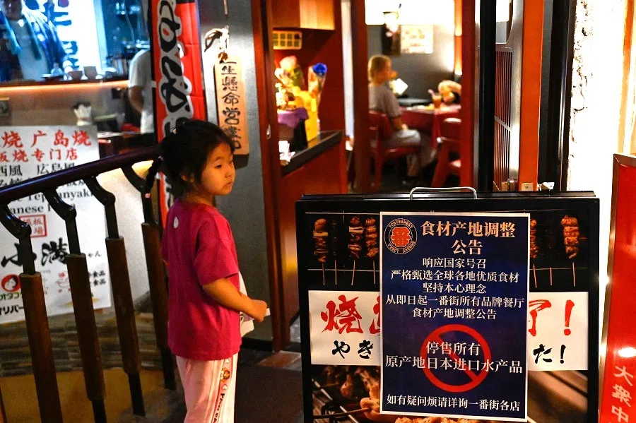 A girl is seen in an area of Japanese restaurants next to a sign reading "Suspend the sale of all fish products imported from Japan", in Beijing, China, on 27 August 2023. (Pedro Pardo/AFP)