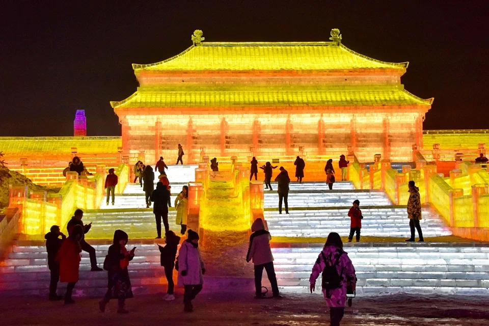 This photo taken on 11 December 2020 shows tourists looking at an illuminated ice sculpture at the Changchun ice and snow grand world in Changchun, Jilin province, China. (STR/AFP)