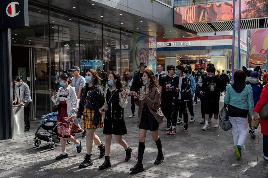 People wearing face masks walk outside a shopping mall during the country's national "Golden Week" holiday in Beijing on 2 October 2020. (Nicolas Asfouri/AFP)