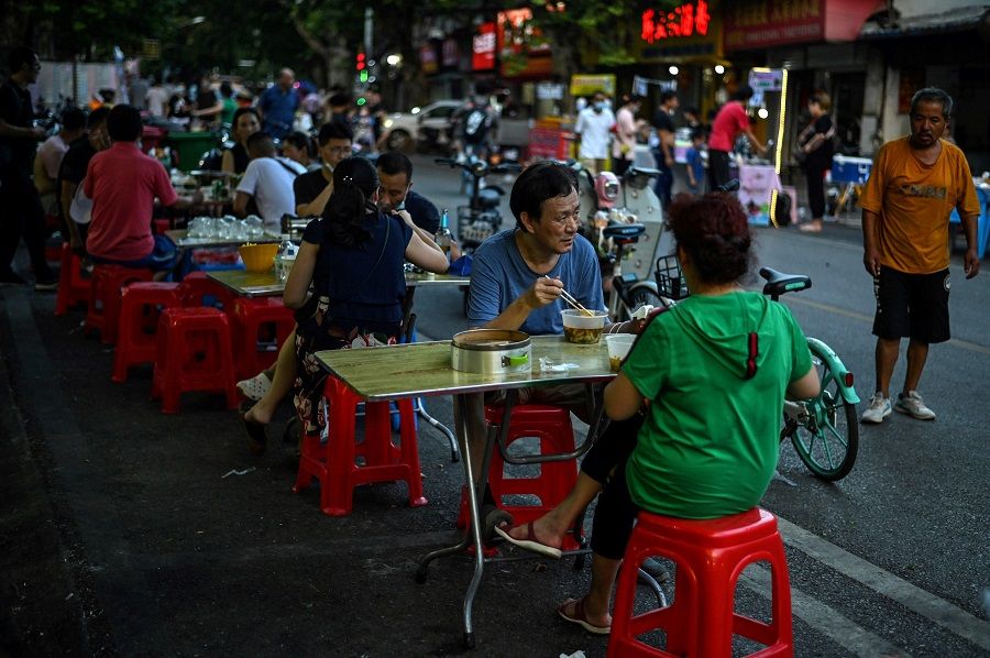 This file photo taken on 5 August 2020 shows people eating during the afternoon in front of a small restaurant in Wuhan, Hubei, China. (Hector Retamal/AFP)