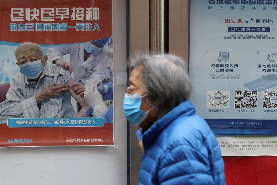 A person walks past a poster encouraging elderly people to get vaccinated against Covid-19, near a residential compound in Beijing, China, 30 March 2022. (Tingshu Wang/File Photo/Reuters)