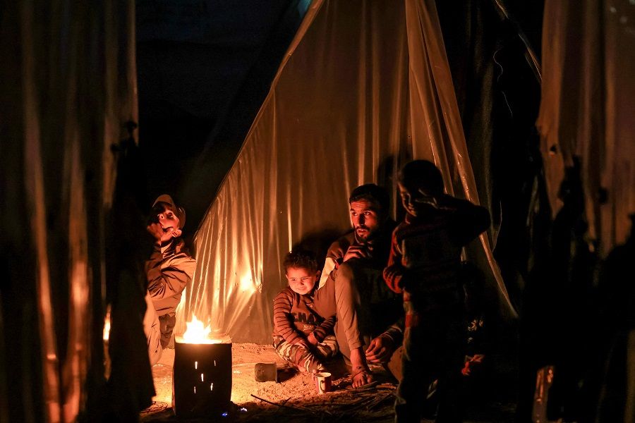 A man sits with children by a fire outside one of the tents housing Palestinians displaced by the conflict in Gaza between Israel and Hamas, in Rafah in the southern Gaza Strip on 18 December 2023. (Mahmud Hams/AFP)