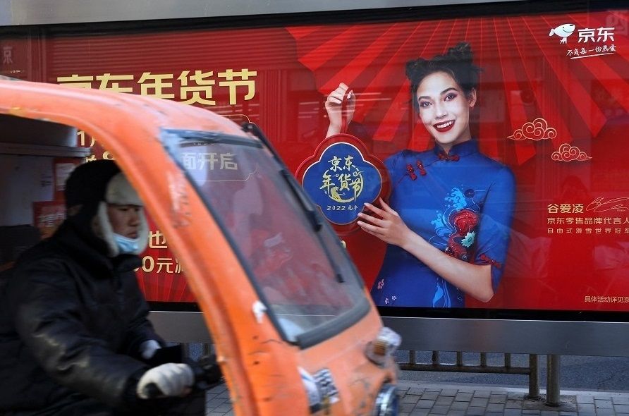 A delivery worker rides a vehicle pasts a JD.com advertisement with an image of freestyle skier Eileen Gu, at a bus stop in Beijing, China, 11 January 2022. (Tingshu Wang/Reuters)