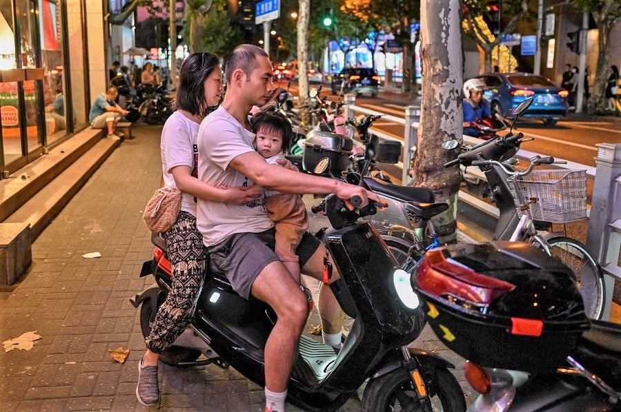 A couple with a child ride on a scooter in Shanghai, China, on 7 September 2021. (Hector Retamal/AFP)