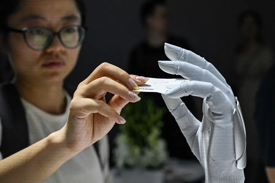 A woman gives a card to a hybrid-driver hand by Xynova Technology during the World Artificial Intelligence Conference (WAIC) in Shanghai on 18 July 2026.