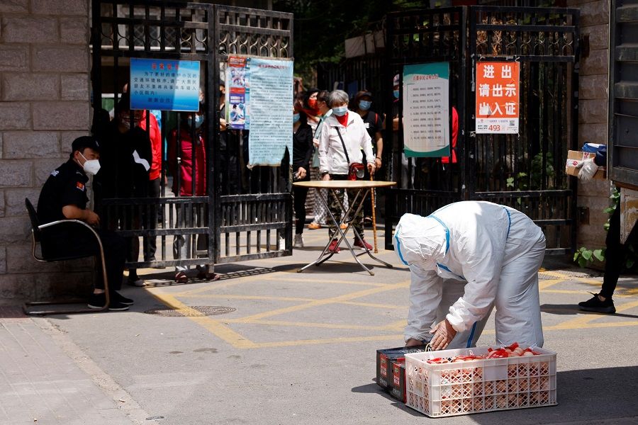 A worker in a protective suit unloads groceries from a truck, as residents in a residential compound under lockdown look on, amid the Covid-19 outbreak in Beijing, China, 17 May 2022. (Carlos Garcia Rawlins/Reuters)