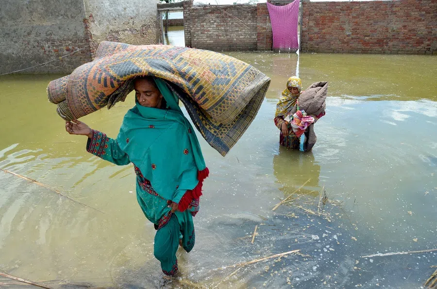 Women displaced by flood, carry their belongings as they wade through floodwaters after heavy monsoon rains at Sohbatpur in Jaffarabad district, Balochistan province, on 19 August 2024. (Fida Hussain/AFP)