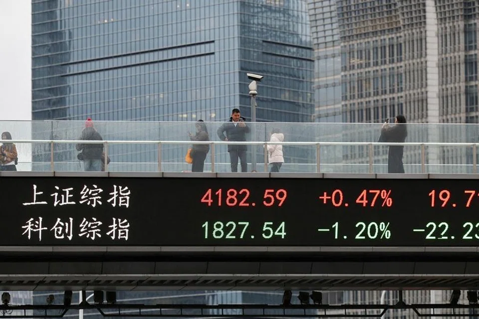 An electronic board shows Shanghai stock indices as people walk on a pedestrian bridge in the Lujiazui financial district in Shanghai, China, on 2 March 2026. (Go Nakamura/Reuters)