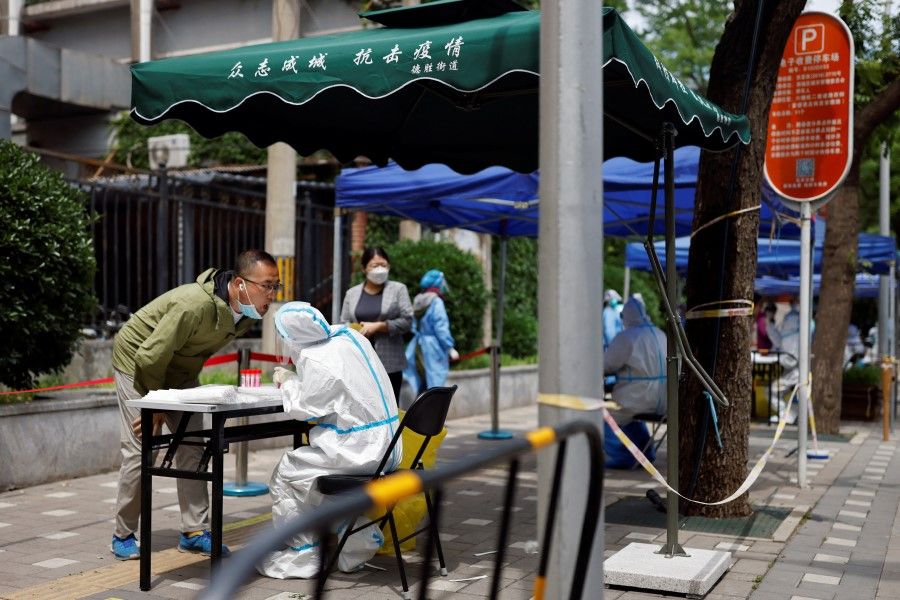 A worker in a protective suit collects a swab from a resident at a makeshift nucleic acid testing site amid the Covid-19 outbreak, in Beijing, China, 9 May 2022. (Carlos Garcia Rawlins/Reuters)
