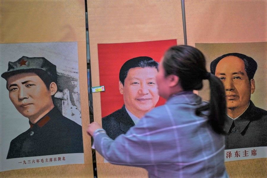 This picture taken during a government organised media tour shows a seller holding a portrait of the Chinese President Xi Jinping next to pictures of the former Chinese leader Mao Zedong at Dongfanghong Theatre in Yan'an, the headquarters of the Chinese Communist Party from 1936 to 1947, in Shaanxi province on 10 May 2021. (Hector Retamal/AFP)