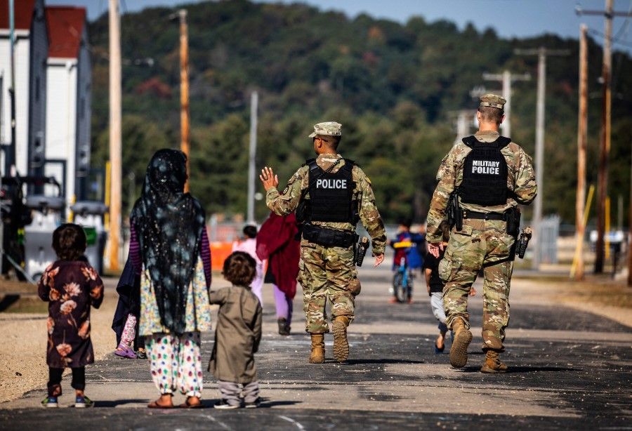 US Military Police walk past Afghan refugees at the Village at the Ft. McCoy US Army base on 30 September 2021 in Ft. McCoy, Wisconsin. (Barbara Davidson/AFP)
