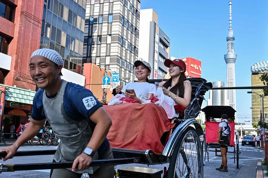 Two young women take a rickshaw ride across from Sensoji Temple in the Asakusa district as the Tokyo Skytree looms in the background in central Tokyo on 16 September 2025. (Richard A. Brooks/AFP)