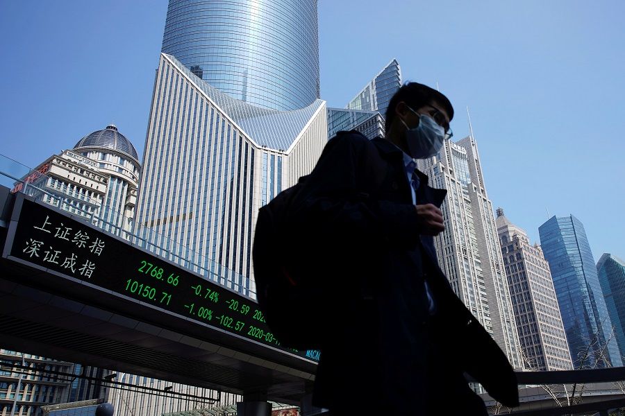 A pedestrian wearing a face mask walks near an overpass with an electronic board showing stock information, at Lujiazui financial district in Shanghai, China, 17 March 2020. (Aly Song/File Photo/Reuters)