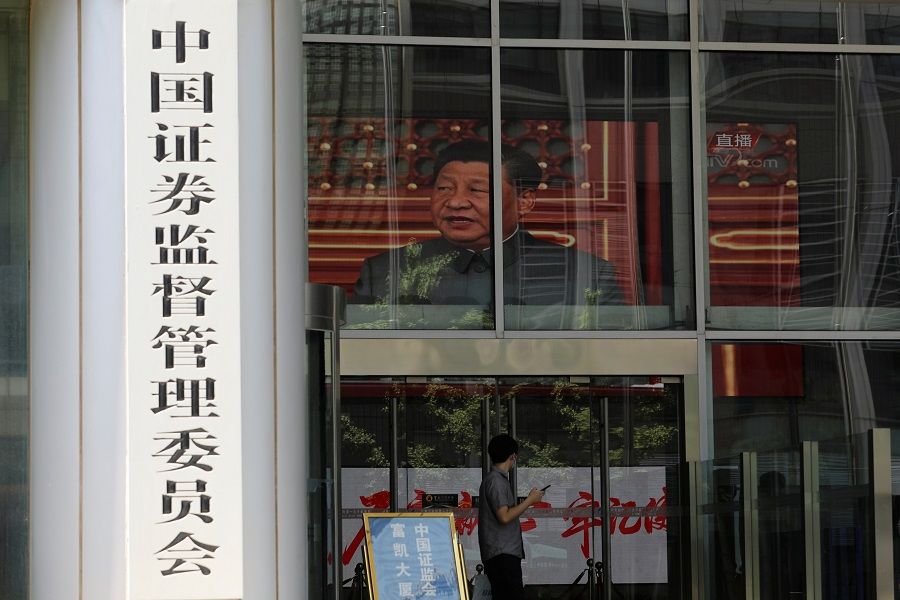 A man stands near a screen showing news footage of Chinese President Xi Jinping at the China Securities Regulatory Commission (CSRC) building on the Financial Street in Beijing, China, 9 July 2021. (Tingshu Wang/Reuters)