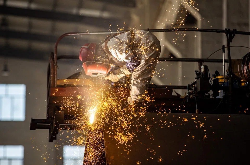 An employee works on a large construction equipment at a factory in Haian, Jiangsu province, China, on 16 October 2023. (AFP)