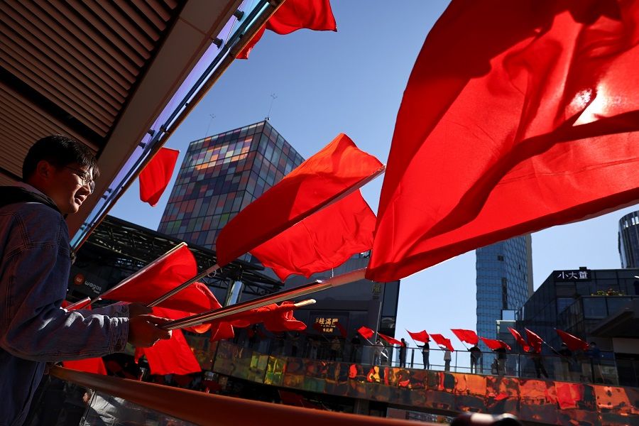 People wave red flags during the filming of a Chinese Communist Party propaganda video in an upscale shopping district in the Sanlitun area in Beijing, China, 19 October 2021. (Thomas Peter/Reuters)