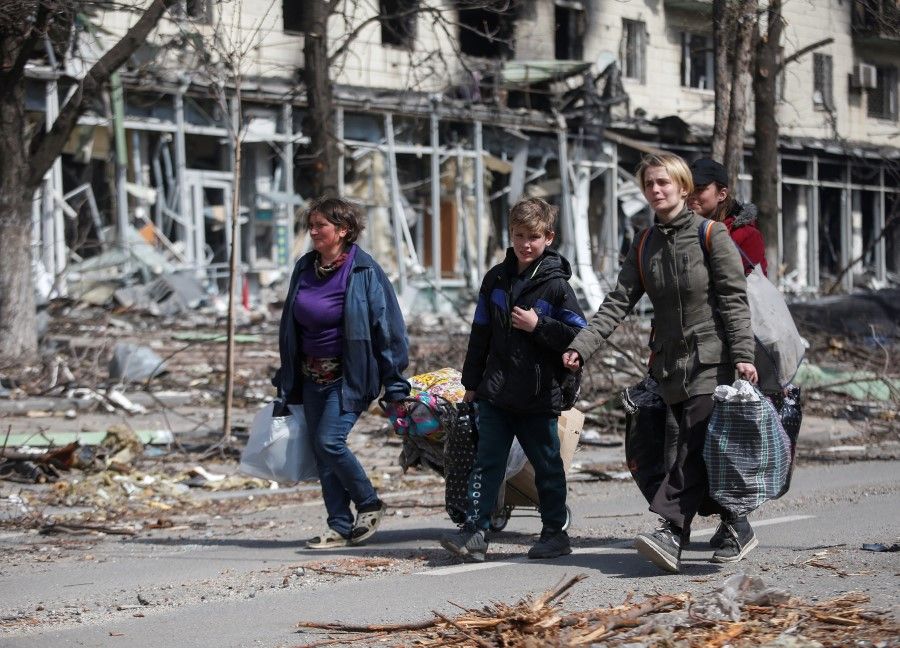 Residents carry their belongings along a street near a building burnt in the course of the Ukraine-Russia conflict, in the southern port city of Mariupol, Ukraine, 10 April 2022. (Alexander Ermochenko/Reuters)