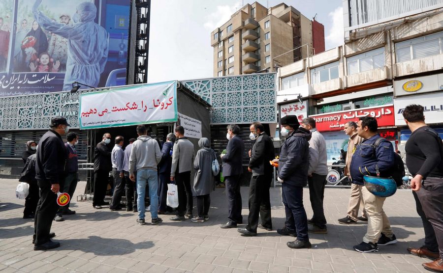 People queue in line to receive packages for precautions against the Covid-19 coronavirus provided by the Basij, a militia loyal to Iran's Islamic republic establishment, from a booth outside Meydan-e Vali Asr metro station in the capital Tehran on 15 March 2020. (STRINGER/AFP)