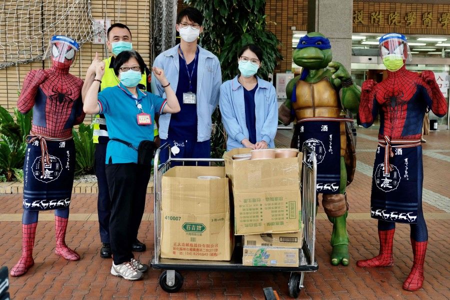 Jimmy Cheng (right), a local restaurant owner dressed as Spider Man, and his consumers fans pose for photographs with medical staffers outside the National Taiwan University Hospital while donating lunch boxes in Taipei on 30 May 2021. (Sam Yeh/AFP)
