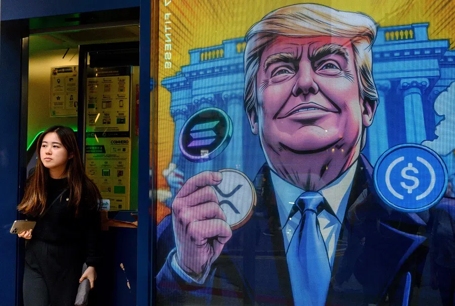 People walk past a cryptocurrency exchange office with a screen featuring US President Donald Trump holding cryptocurrency coins in Hong Kong on 12 March 2025.