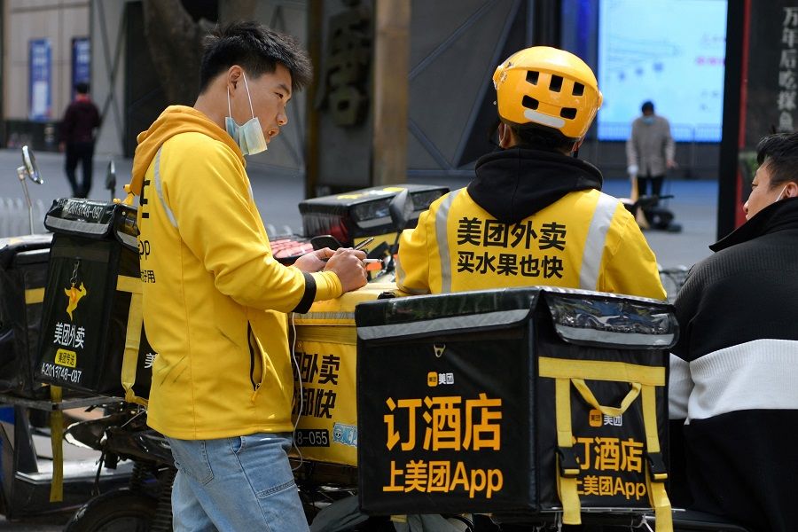 Delivery riders for Meituan, one of China's biggest food delivery firms, chat while waiting for orders outside a restaurant in Beijing, China on 27 April 2021. (Greg Baker/AFP)