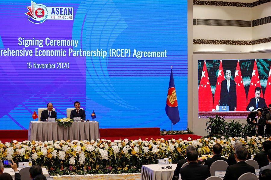 Vietnam's Prime Minister Nguyen Xuan Phuc (left) sits next to Minister of Industry and Trade Tran Tuan Anh as they watch a screen showing Chinese Minister of Commerce Zhong Shan (right) signing next to Chinese Premier Li Keqiang during the virtual signing ceremony of the Regional Comprehensive Economic Partnership (RCEP) Agreement during the 37th ASEAN Summit in Hanoi, Vietnam, 15 November 2020. (Kham/Reuters)