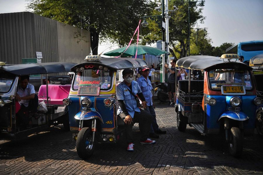 In this photo taken on 17 February 2020, a tuk tuk driver in a protective facemask, amid fears over the spread of the Covid-19 coronavirus, waits for customers near the Grand Palace in Bangkok. (Lillian Suwanrumpha/AFP)