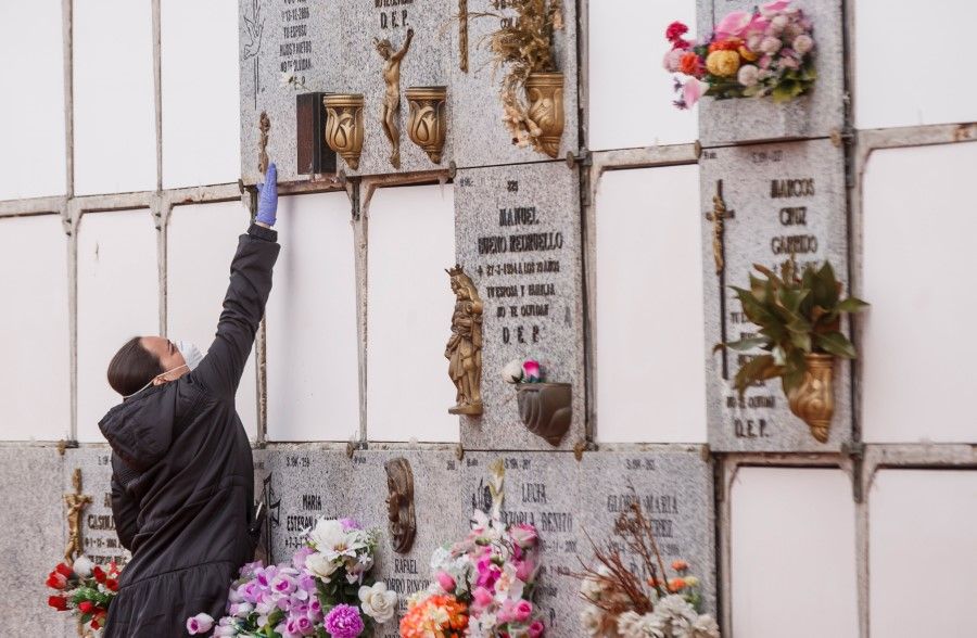 A woman touches a niche during the burial of a man who died of Covid-19 at the South Municipal cemetery in Madrid, March 23, 2020. (Baldesca Samper/AFP)
