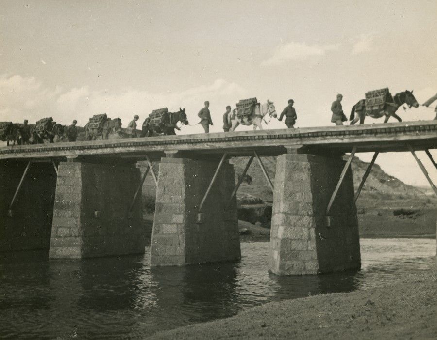 Chinese artillery soldiers leading horses across a bridge.