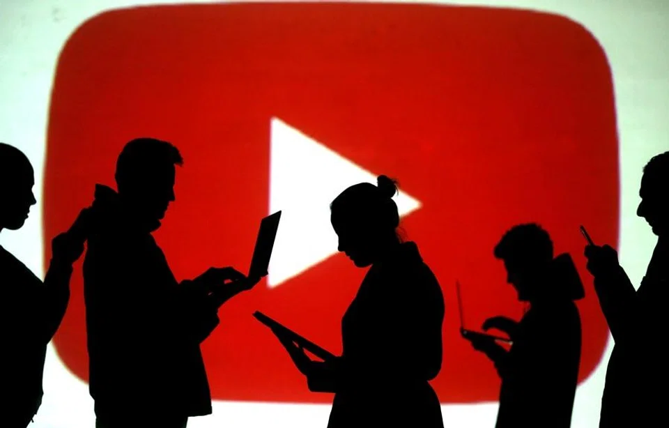Silhouettes of laptop and mobile device users are seen next to a screen projection of the YouTube logo in this picture illustration taken on 28 March 2018. (Dado Ruvic/Illustration/Reuters)