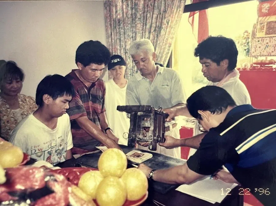 My father (fifth from left), holding one side of the spirit-medium chair to consecrate paper talismans during a temple service, Brunei, 22 December 1996.