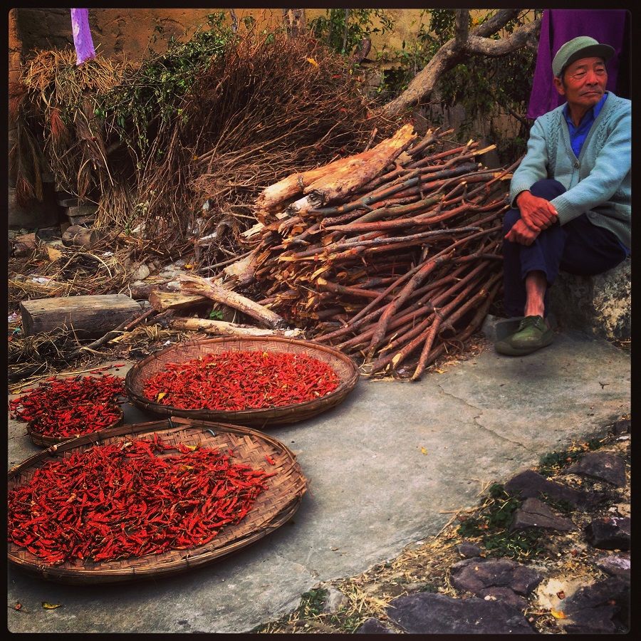 Displaying his dried red chilies in woven bamboo baskets along a village lane, this farmer in Yuanyang, Yunnan awaits buyers.