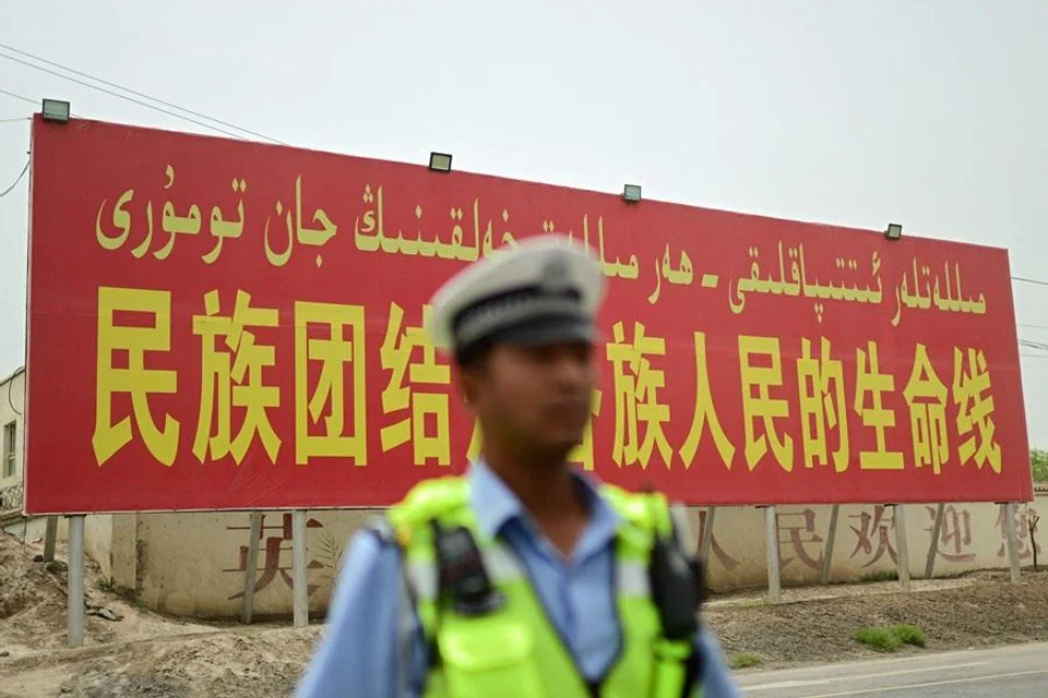 This photo taken on 19 July 2023 shows a policeman standing in front of a billboard that reads, “National unity is the lifeline for people of all ethnic groups”, on a road in Kashgar prefecture, in China's Xinjiang region. (Pedro Pardo/AFP)