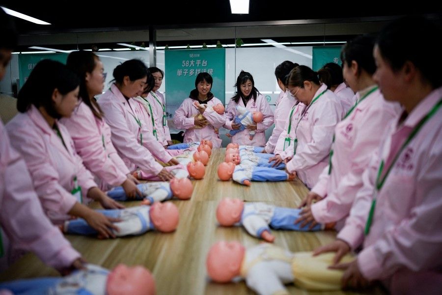 Women train with plastic baby dolls as they take part in a nursing skills class for confinement carers, at Yipeitong training centre in Shanghai, China, 2 March 2023. (Aly Song/Reuters)