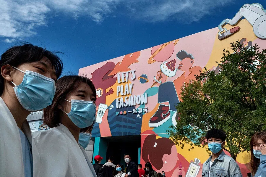 People wearing face masks as a preventive measure against the Covid-19 coronavirus walk outside a shopping mall complex during the country's national "Golden Week" holiday in Beijing on 2 October 2020. (Nicolas Asfouri/AFP)